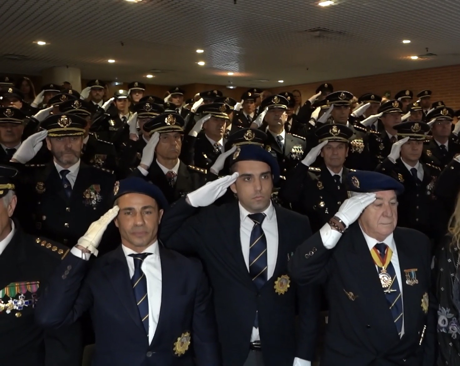 Socios con boina y blazer saludando en formación durante un acto